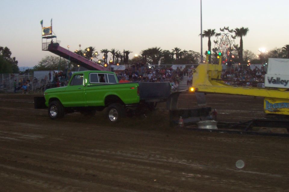 Green pickup truck with chrome wheels and a lifted suspension, towing a yellow trailer. The truck has a stepside bed and a single cab