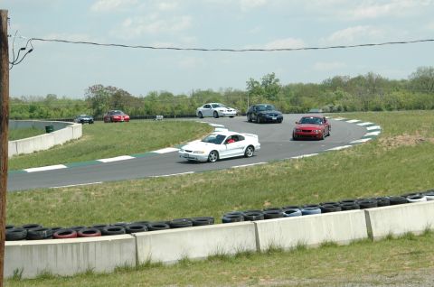 1993 Ford Mustang - Multiple vehicles compete on a winding race track under a cloudy sky.