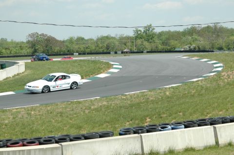 1993 Ford Mustang - A white coupe with a GT-40 decal drives on a race track, with other vehicles in the background.