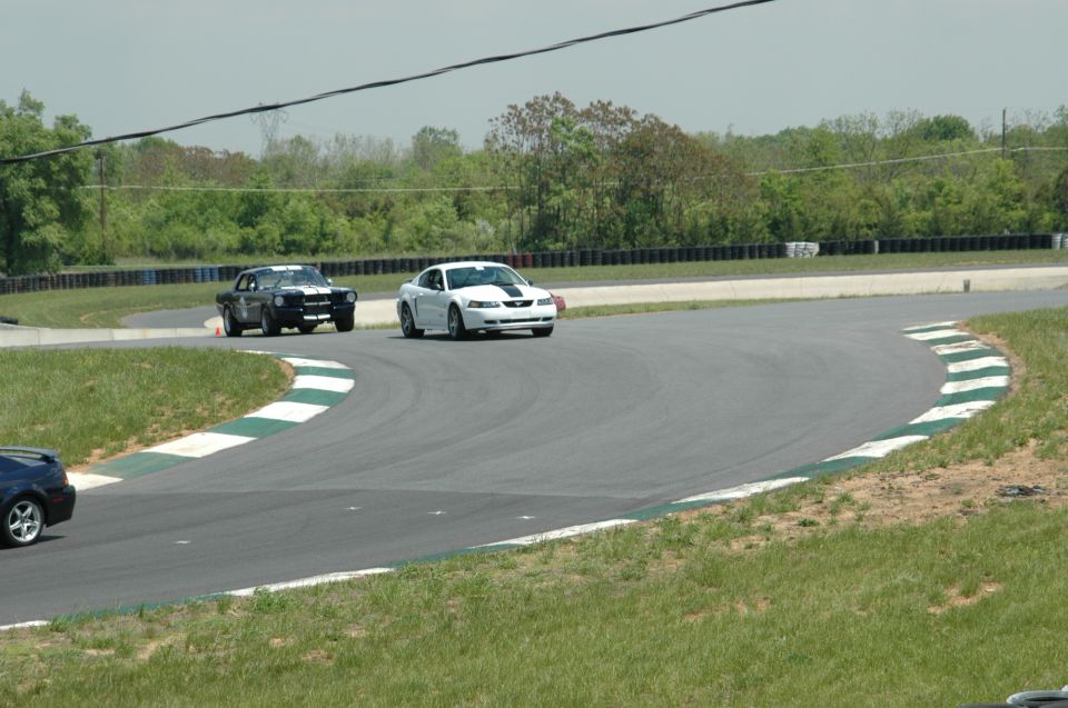 White Ford Mustang with black racing stripes on a track, 3q-front view