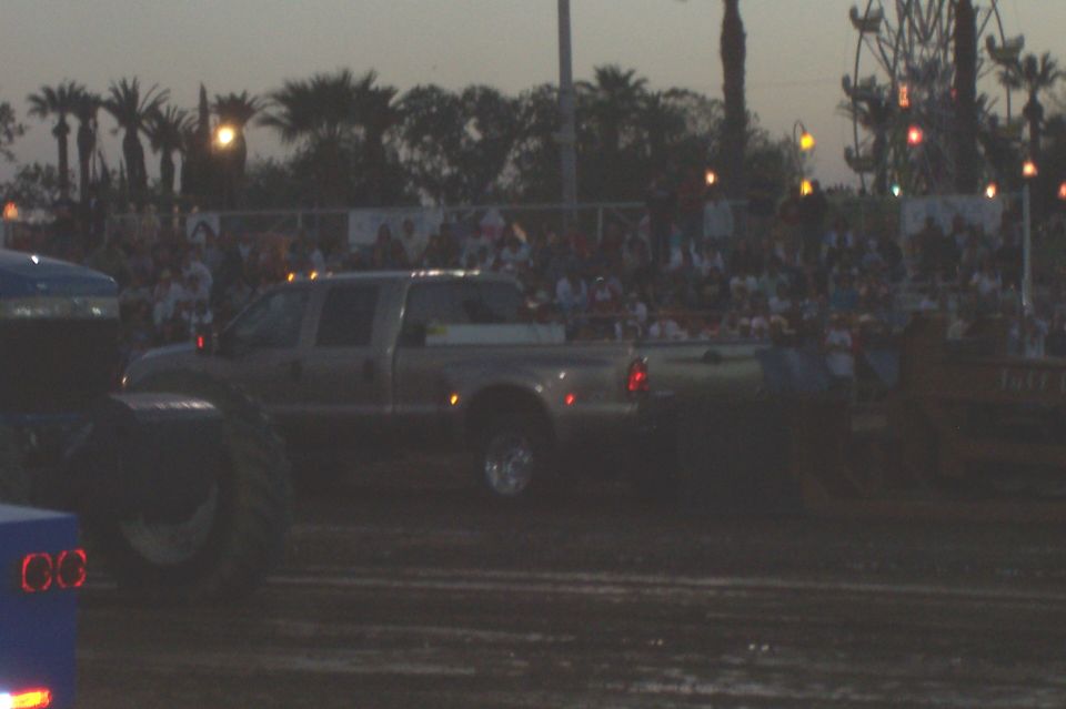 Pickup truck with dual rear wheels in a dirt field, crowd in background