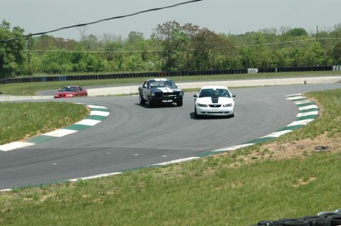 1993 Ford Mustang - Cars compete on a winding race track under a cloudy sky.
