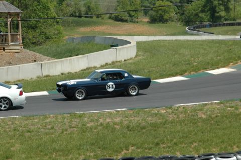 1993 Ford Mustang - A dark blue coupe with white racing stripes and the number 84 on its side drives on a track.