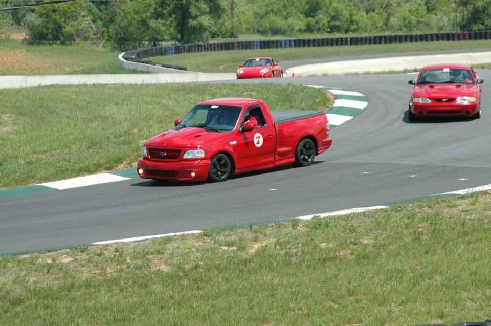 Red pickup truck with racing number 7 on a track, with two red cars in the background