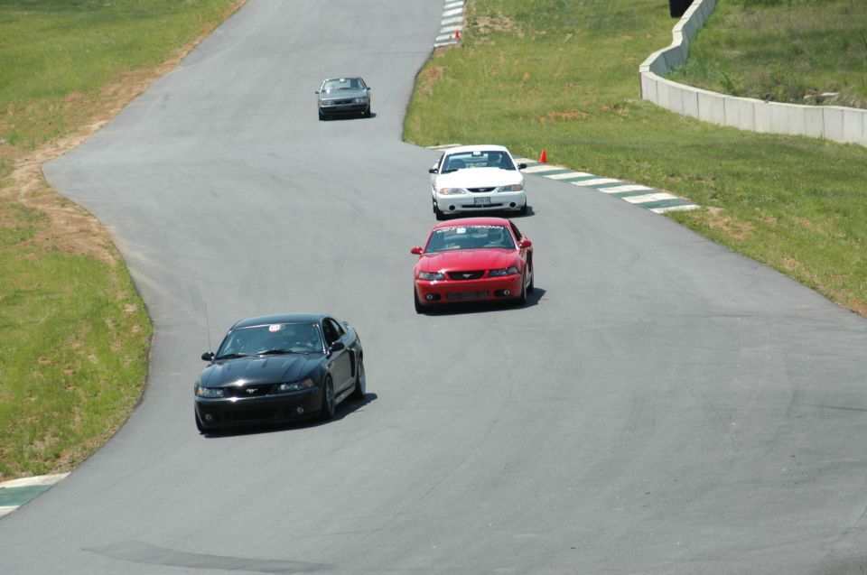 Black, red, and white Mustangs on a race track with a fourth car behind them