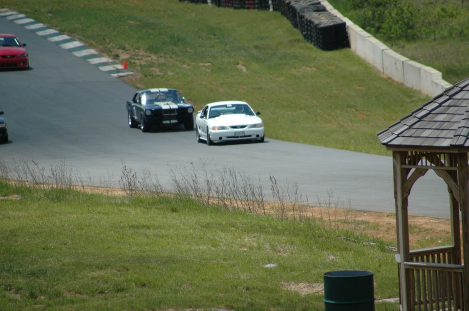 White 1996 Ford Mustang GT on a race track, with a black classic Mustang and a red car visible