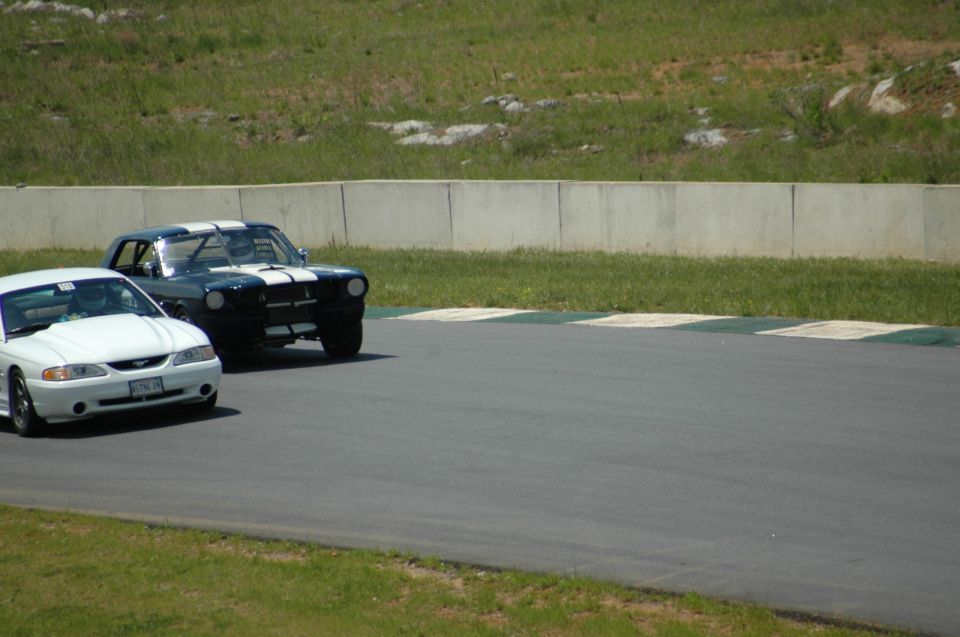 White 1994 Ford Mustang in foreground, dark blue classic Mustang with white stripes behind it on a race track