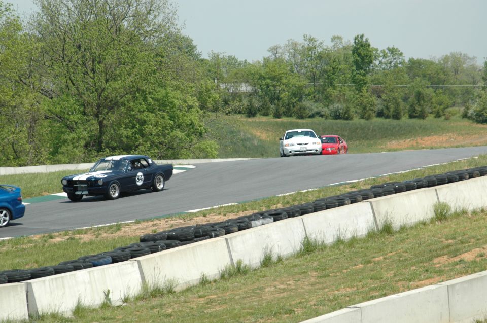 Dark blue classic Mustang with white stripes and number 52 on track, followed by white and red cars