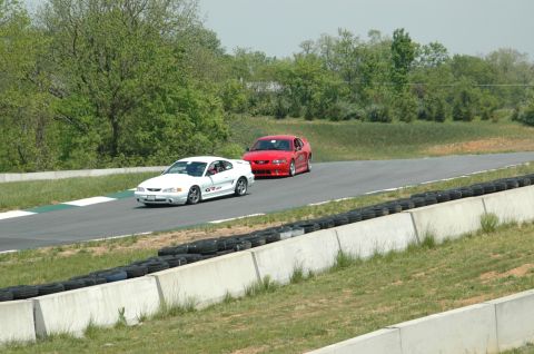 1993 Ford Mustang - Two Ford Mustangs are seen on a race track during a sunny day.