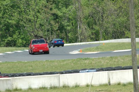 1993 Ford Mustang - Two vehicles navigate a turn on a paved racetrack surrounded by trees.