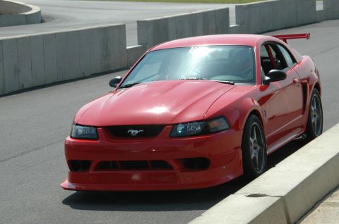 1993 Ford Mustang - A red Ford Mustang with a large rear spoiler is parked on the side of a race track.