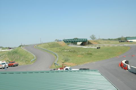 1993 Ford Mustang - A race track scene a bridge and various support vehicles on the side of the track.