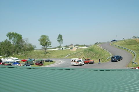 1993 Ford Mustang - A sunny day at the race track features an RV, tents, and several vehicles including an ambulance and tow truck.