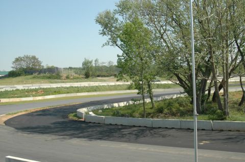 1993 Ford Mustang - A distant white car drives on a race track surrounded by trees and concrete barriers on a clear day.