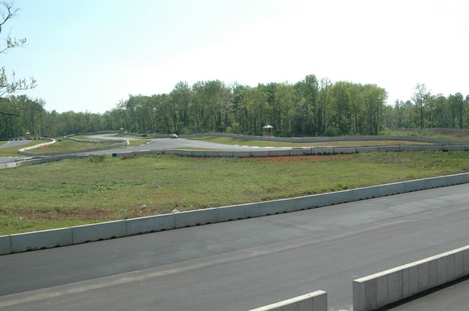 Race track with concrete barriers and green grass, a distant car is visible on the track