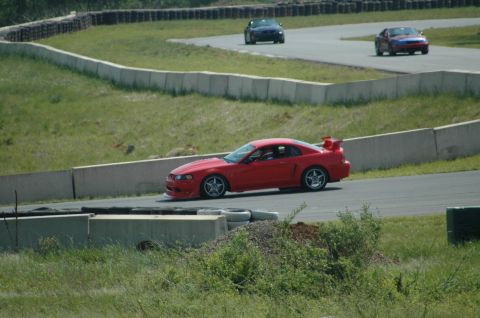 1993 Ford Mustang - A red sports car navigates a turn on a race track, with other vehicles in the background.