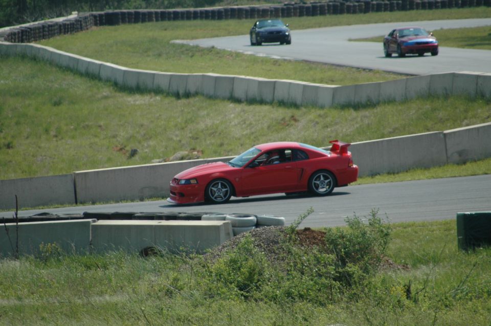 Red sports car with a rear spoiler on a race track, viewed from the front-right