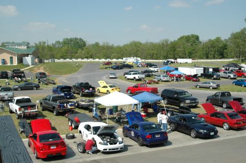 1993 Ford Mustang - A red coupe, possibly a 2000 model, is parked with its hood open at a track event.