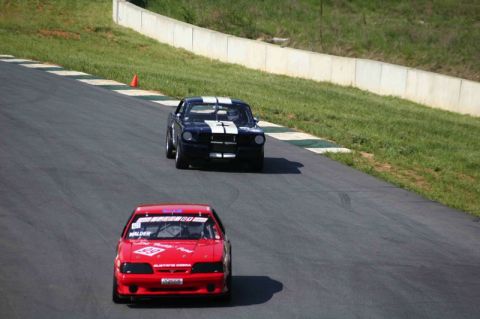 1993 Ford Mustang - Two Ford Mustangs, one red and one black with white stripes, compete on a race track.