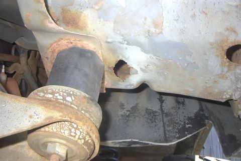 1994 Ford Bronco - Close-up view of a heavily rusted vehicle frame, showing suspension components and a hole in the metal.