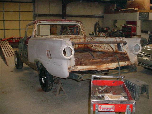 Primer-gray vintage Ranchero pickup with rusty bed on jack stands in a shop