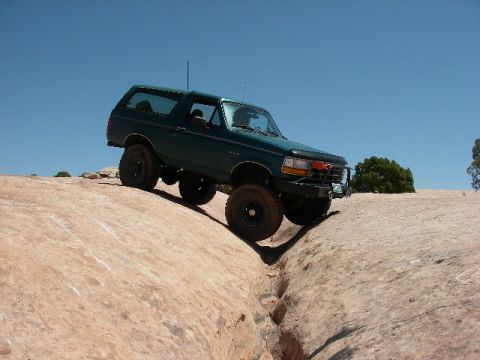 1996 Ford Bronco - A green 1996 Ford Bronco navigates a challenging rock formation on a sunny day.