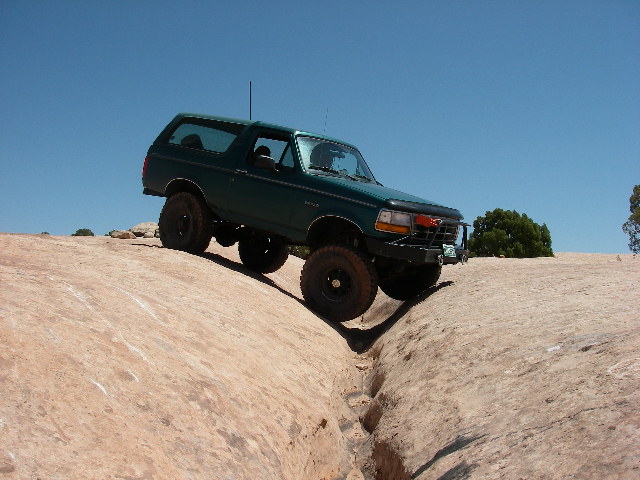 Teal Ford Bronco flexed across a slickrock trough on Seven Mile Rim, Moab