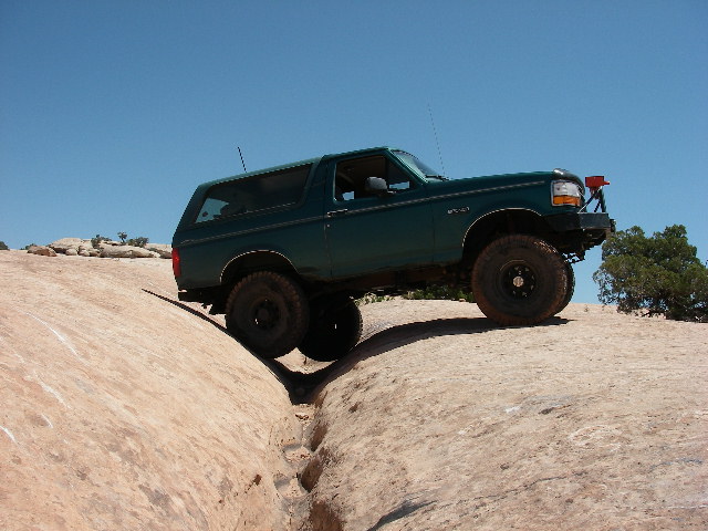 Green Ford Bronco straddling a crack in slickrock with black steel wheels