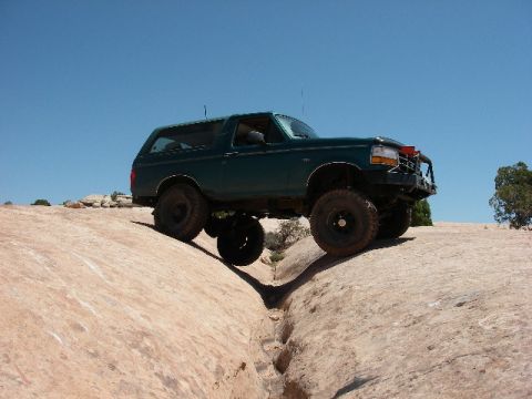 1996 Ford Bronco - This 1996 Ford Bronco navigates a challenging off-road obstacle under a clear blue sky.