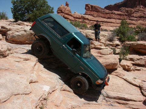 1996 Ford Bronco - An SUV is shown off-roading on a steep, rocky incline under a clear blue sky.