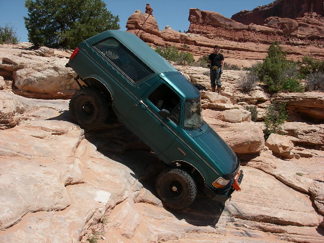 Teal Ford Bronco nose-down on a steep slickrock ledge at Wipe Out Hill, Moab