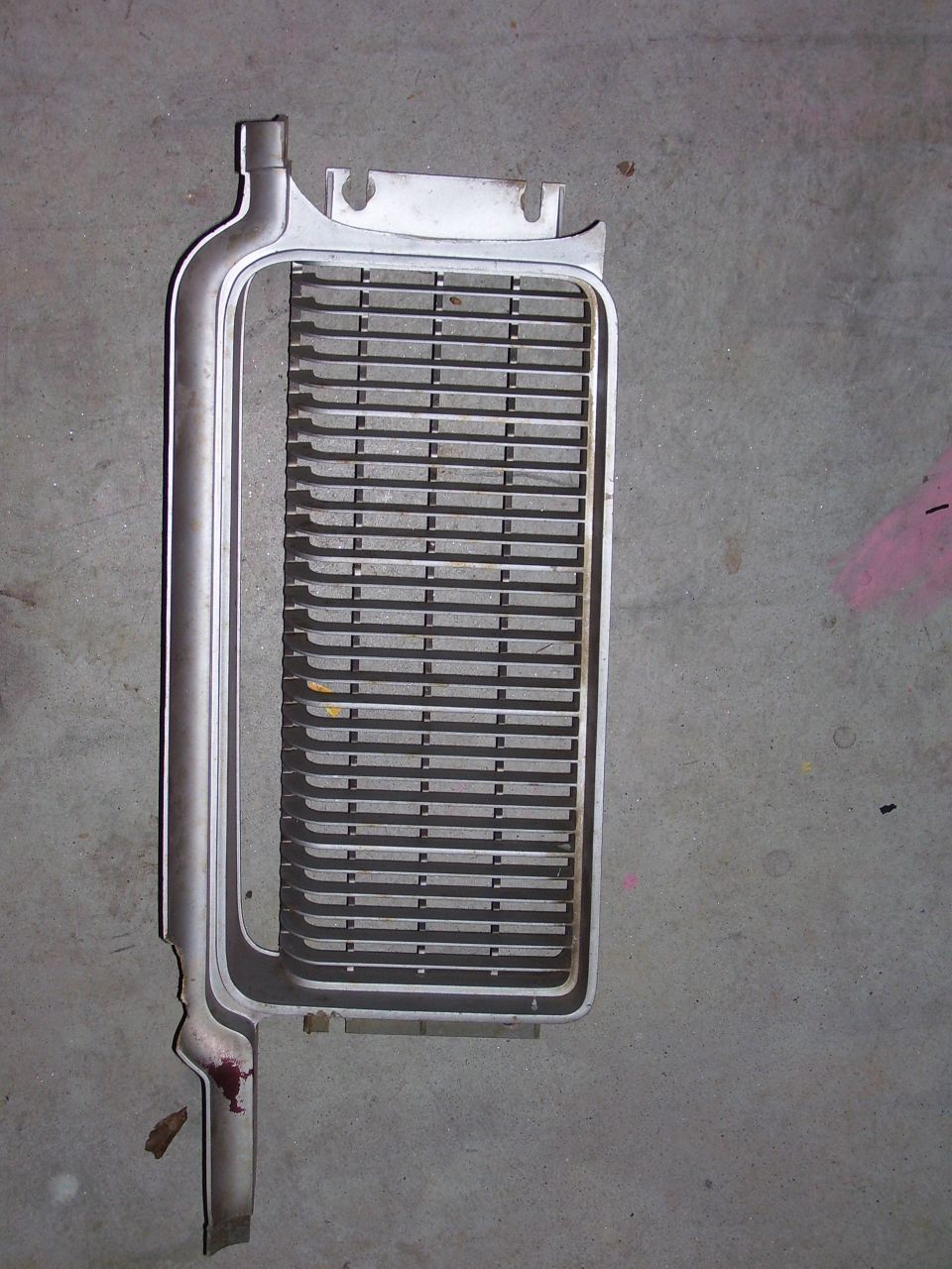 Car grille with horizontal slats, silver colored, lying on a concrete floor