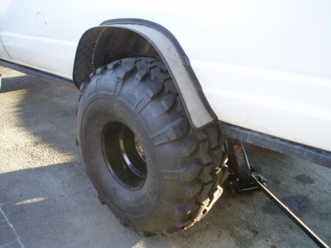2000 Ford E350 - The van has oversized tires and custom fender flares, with a jack positioned to lift the vehicle.