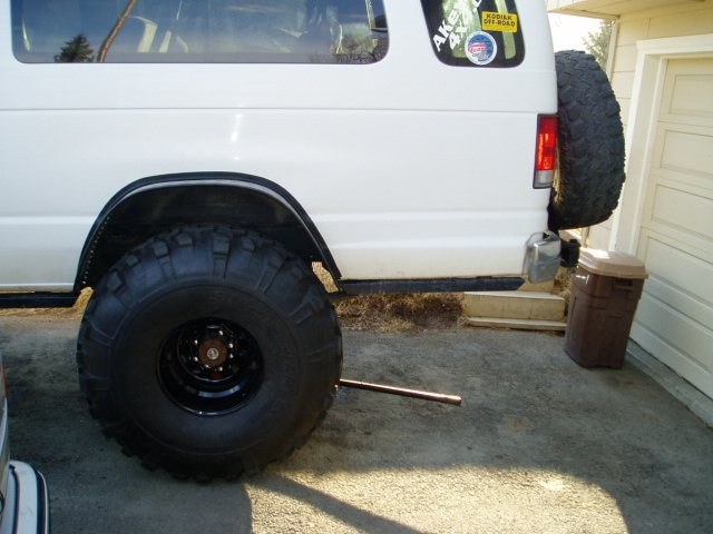 Rear corner of white lifted van with oversized mud tire on black steel wheel