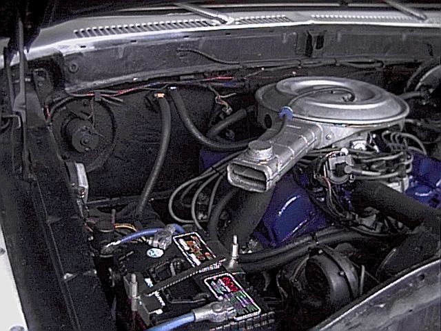 Engine bay with blue-painted V8, chrome air cleaner, black hoses, and battery in foreground