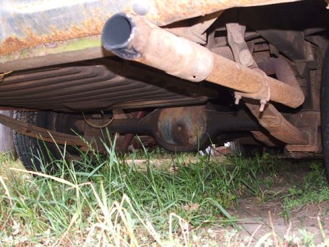 1966 Ford Ranchero - The underside of a vehicle, showing the rear axle, leaf springs, and exhaust system, with grass growing around it.