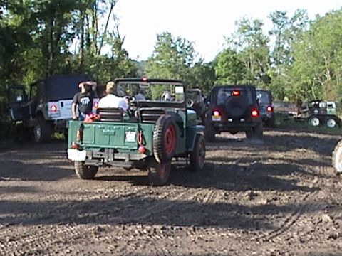 1996 Ford Bronco - Multiple off-road vehicles are parked in a muddy field, with trees lining the background.