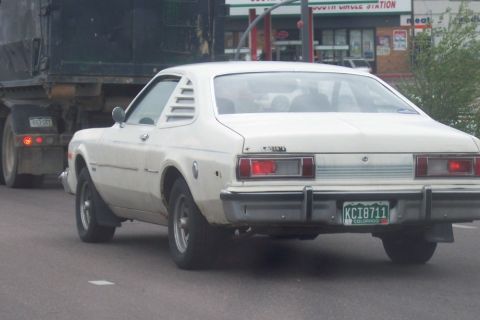 1972 Ford Ranchero - White 1977 Dodge Aspen coupe seen from the rear, following a large truck on the road.