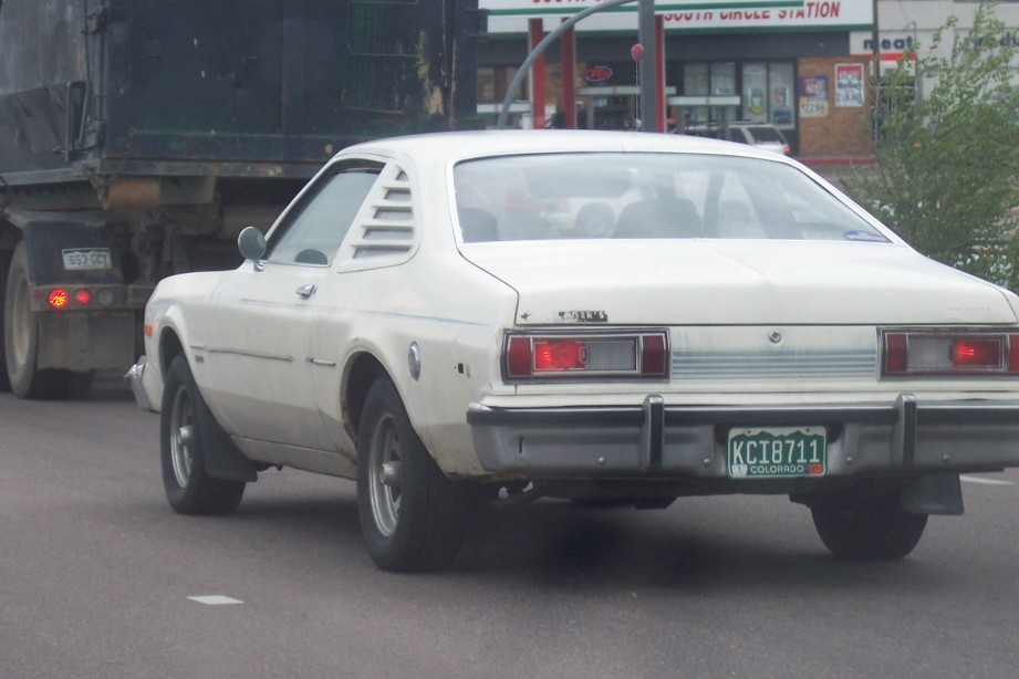 White 1977 Dodge Aspen coupe rear view, driving behind a dark truck. Colorado license plate KC18711