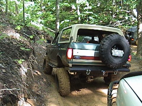 1996 Ford Bronco - A Ford Bronco navigates a wooded trail, with another vehicle visible behind it.