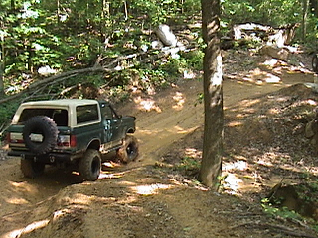 Green 1996 Ford Bronco with spare tire on rear, navigating a muddy off-road trail