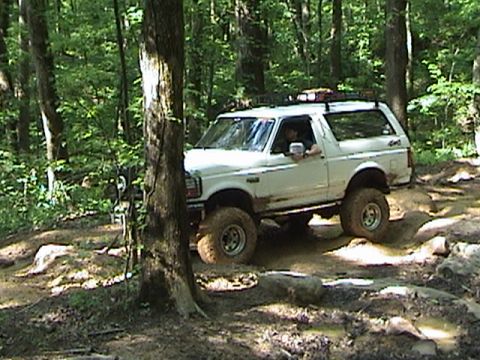 1996 Ford Bronco - A white Ford Bronco navigates a muddy trail in a wooded area.