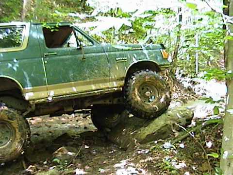 1996 Ford Bronco - This green SUV is navigating a challenging off-road course with muddy terrain and large rocks.