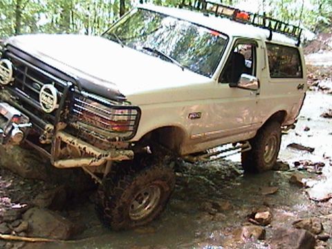 1996 Ford Bronco - White 1996 Ford Bronco navigates a challenging off-road course with mud and water.