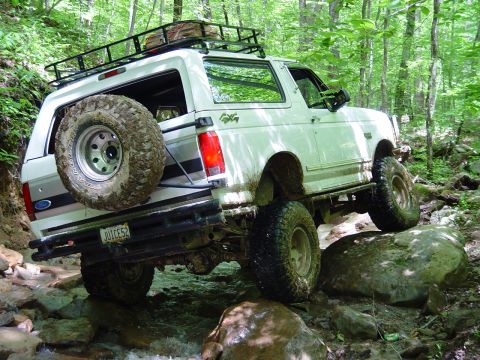 1996 Ford Bronco - A white Ford Bronco navigates a rocky stream bed in a wooded area.