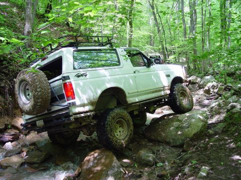 1996 Ford Bronco - A white 1996 Ford Bronco tackles a challenging off-road trail, with a second vehicle visible in the background.