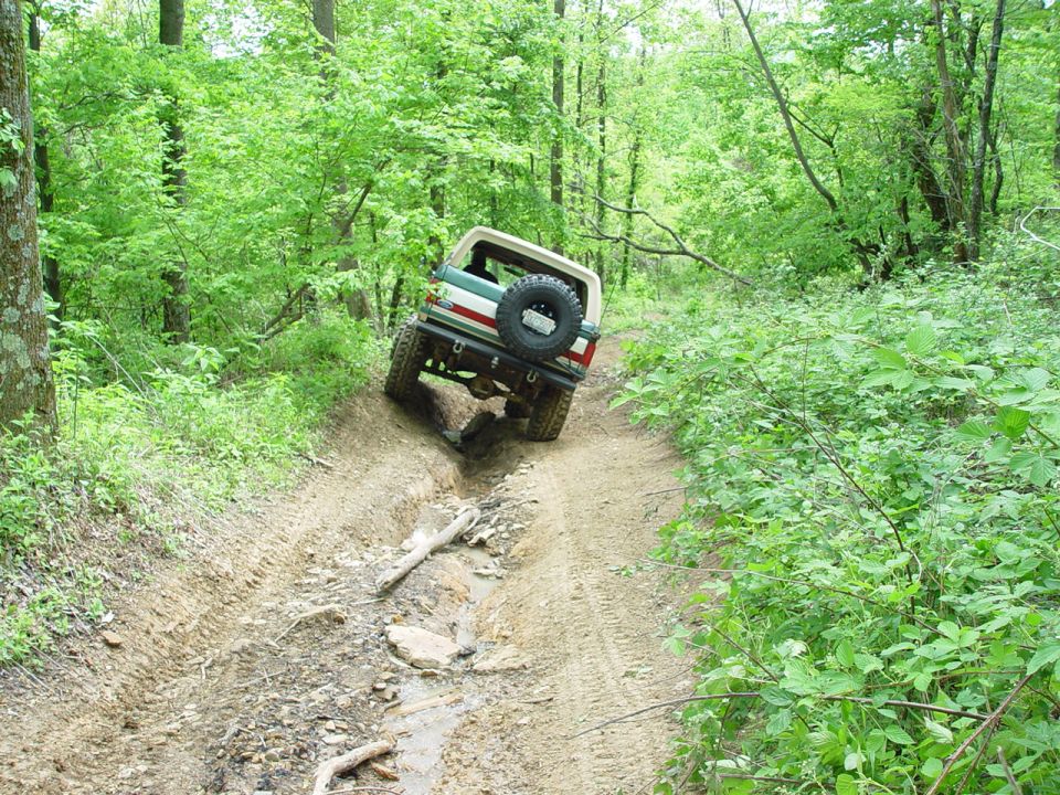 1996 Ford Bronco driving on a muddy, rutted trail through a forest