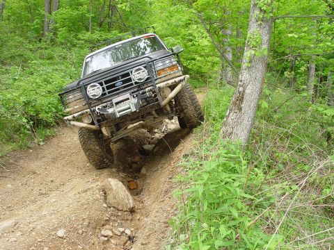1996 Ford Bronco - This modified SUV, likely a 1992 model, tackles a challenging off-road course with its front wheels angled sharply.