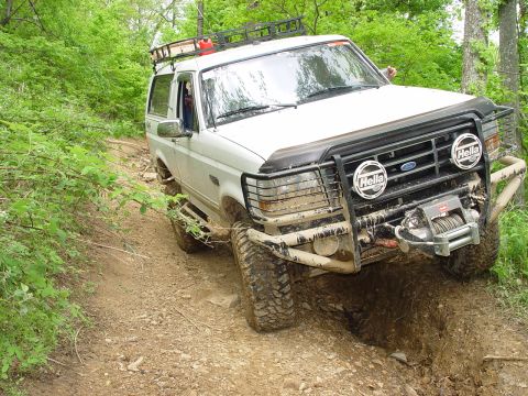 1996 Ford Bronco - This SUV is navigating a muddy, off-road trail with dense foliage on either side.