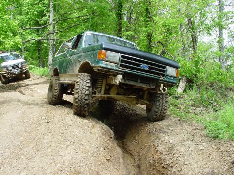 1996 Ford Bronco - A green Ford Bronco tackles a challenging off-road course, with another vehicle visible in the background.